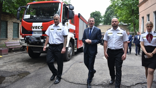 Valsts prezidents ar ugunsdzēsējiem iet pa depo iekšpagalmu, kreisajā pusē ugunsdzēsēju auto