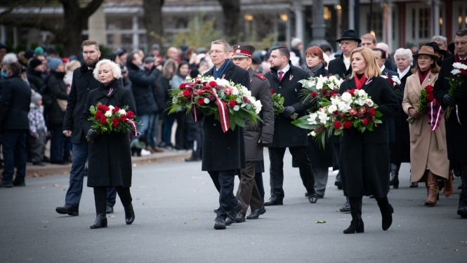 Amatpersonas iet ar ziedu vainagiem rokās