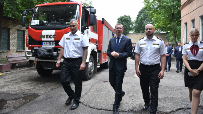 Valsts prezidents ar ugunsdzēsējiem iet pa depo iekšpagalmu, kreisajā pusē ugunsdzēsēju auto
