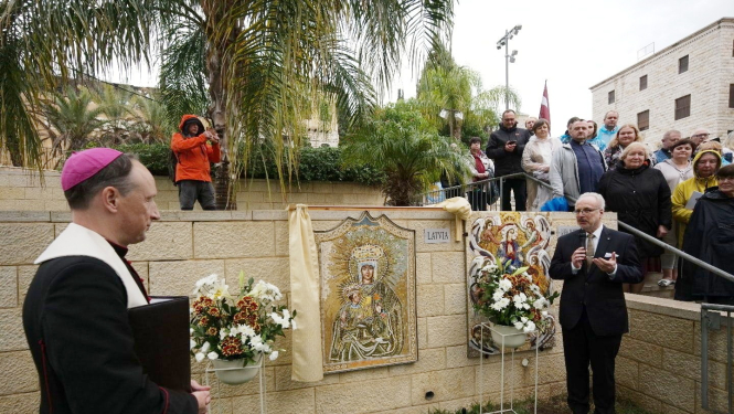 Garīdznieks un Valsts prezidents stāv pie mozaīkas, kas izvietota uz mūra sienas