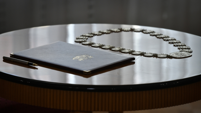 Ilustratīvs foto: uz galda novietota pildspalva, tiesneša zvēresta teksts vākos un tiesneša amata zīme