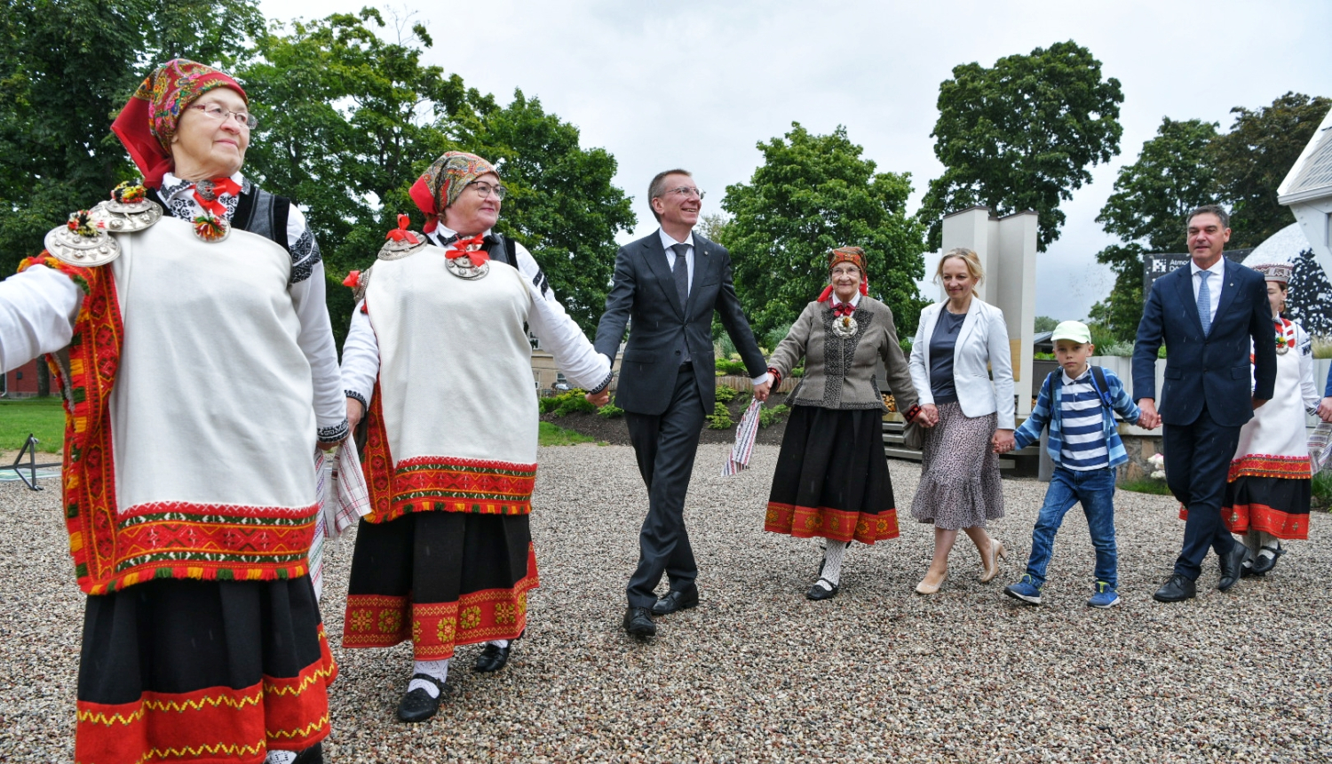 Valsts prezidents sadevies rokās ar tautastērpos ģērbtām suitu sievām iet rotaļā