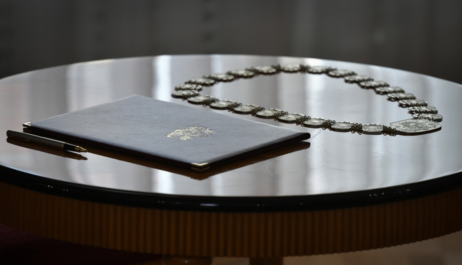 Ilustratīvs foto: uz galda novietota pildspalva, tiesneša zvēresta teksts vākos un tiesneša amata zīme