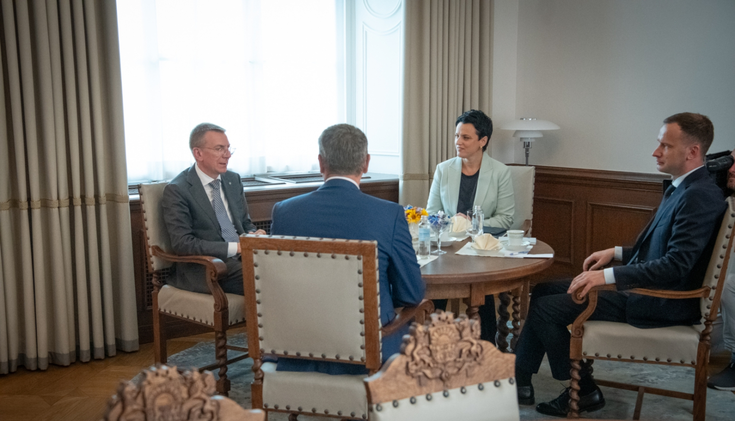 No kreisās: Edgars Rinkēvičs, Gunda Reire, Mārtiņš Drēģeris, Māris Sprindžuks (ar muguru) sēž ap galdu un sarunājas